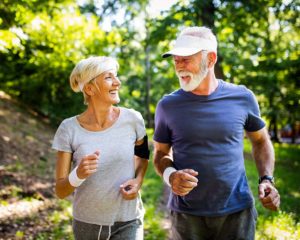 A mature man and woman run along a forest trail