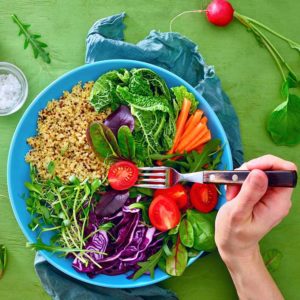 Hand with a fork poised over a bowl of healthy foods such as quinoa, mixed seasonal greens and sprouts