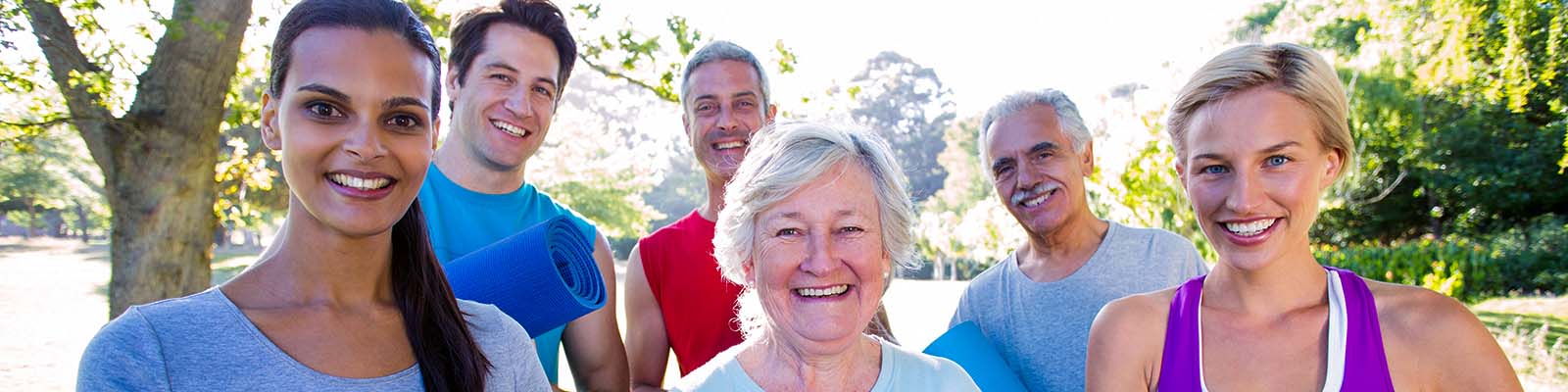 Happy, athletic group holding exercise mats on a sunny day